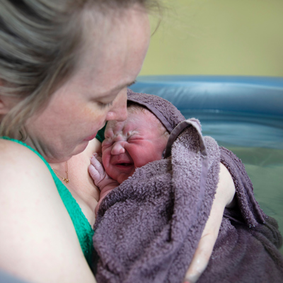 new born baby being held by mother in birthing pool wrapped in towel